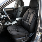 Black electric car seat cushion set installed on the front passenger seat and matching floor cushion, shown inside a car with the door open. A small wired remote control rests on the seat cushion.