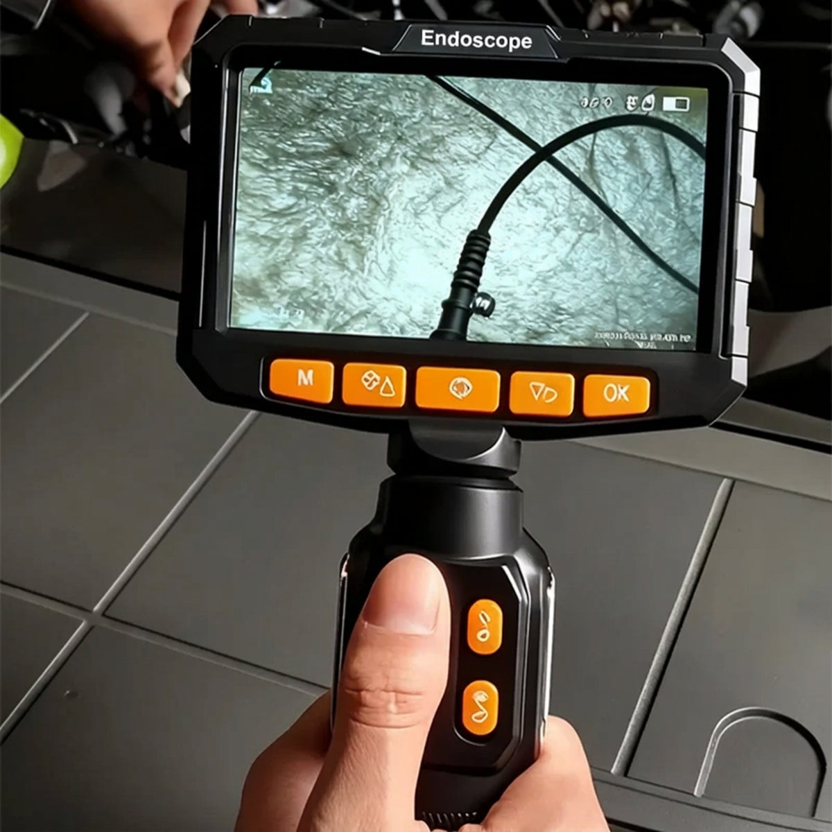 Handheld inspection camera showing the 5-inch live display and orange steering controls during use.