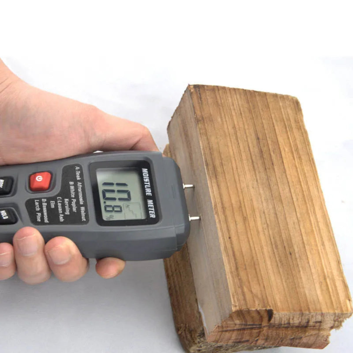 Wood moisture meter used on a timber block, with the reading shown on its LCD display.