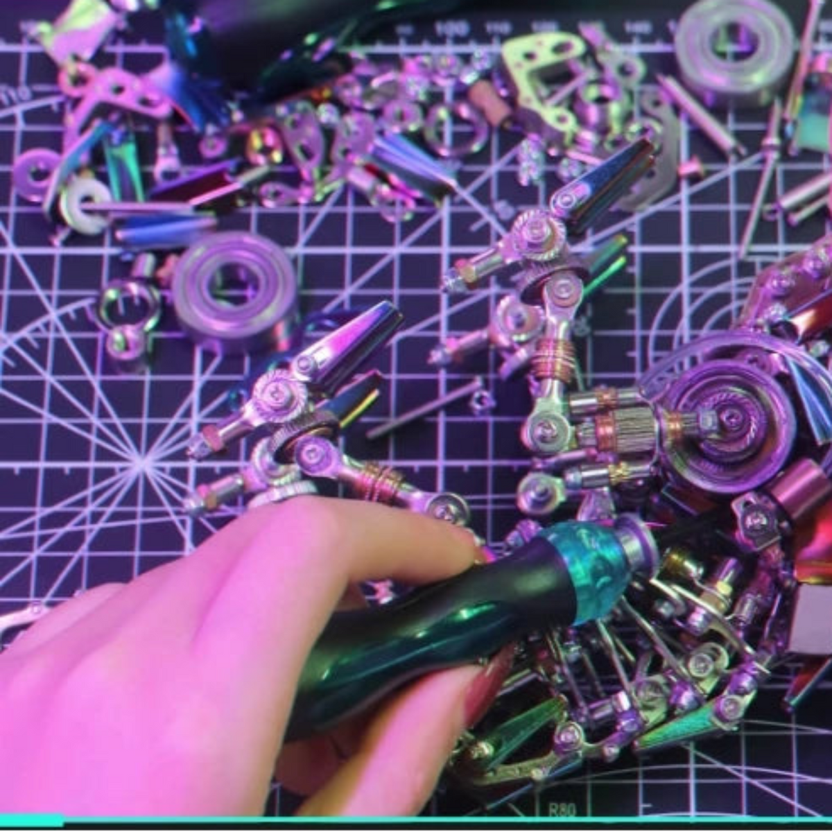 Hands assembling the mechanical chameleon metal model with loose metal components and a screwdriver